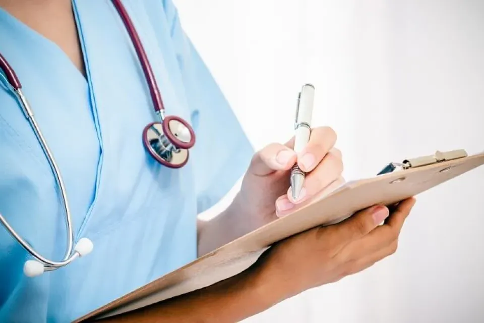 Practical Nurse LPN in Blue Scrubs Taking Notes on Clipboard